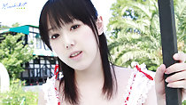 Standin in front of trees tendrils of long hair over her pale shoulders holding onto post