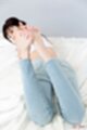 Lying on her front looking back bare feet raised wearing jeans